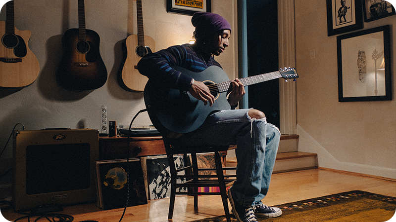 Musician seated and playing an acoustic guitar in a cozy indoor studio setting