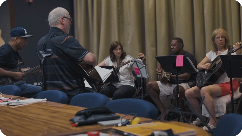 Adult students practicing guitar together in a classroom workshop setting