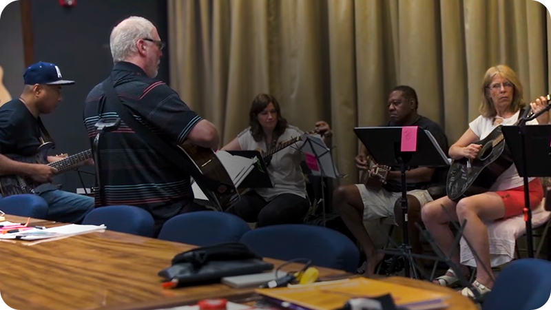Adult students practicing guitar together in a classroom workshop setting