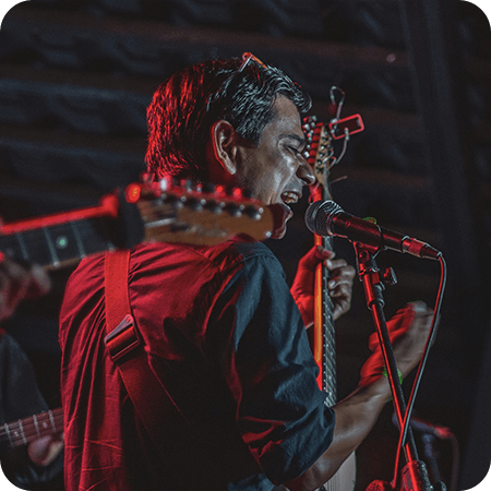 Guitarist performing on stage with a microphone under dramatic red lighting.