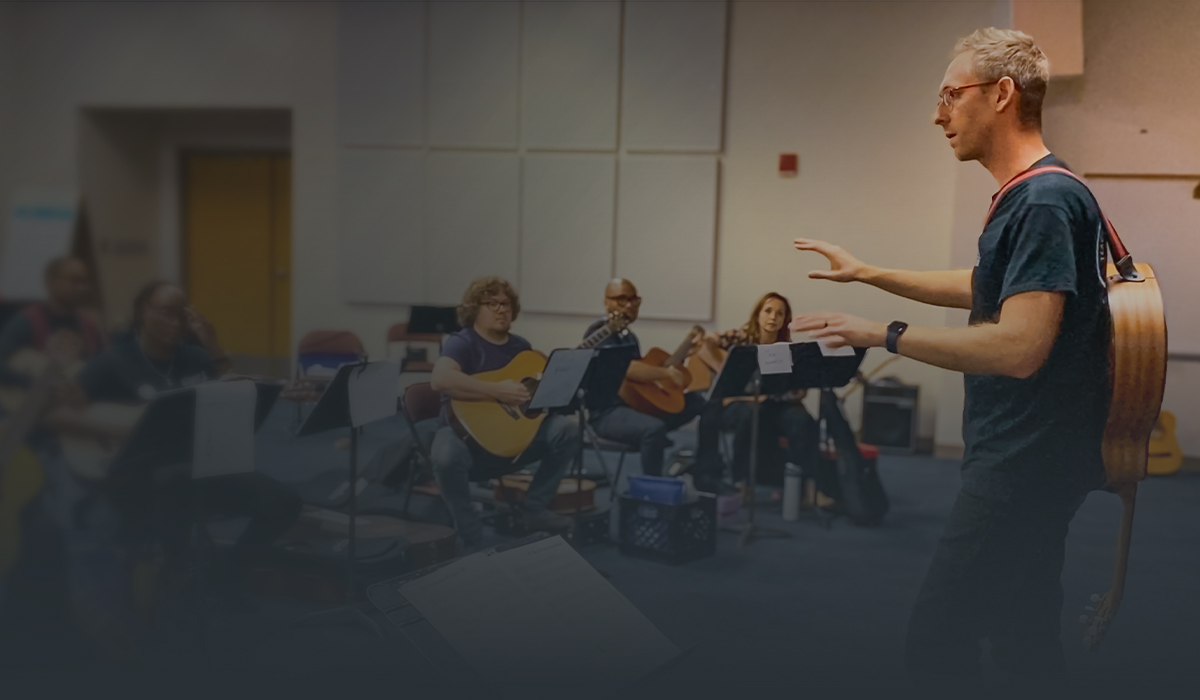 Instructor leading a Teaching Guitar Workshops class with adult students playing guitars