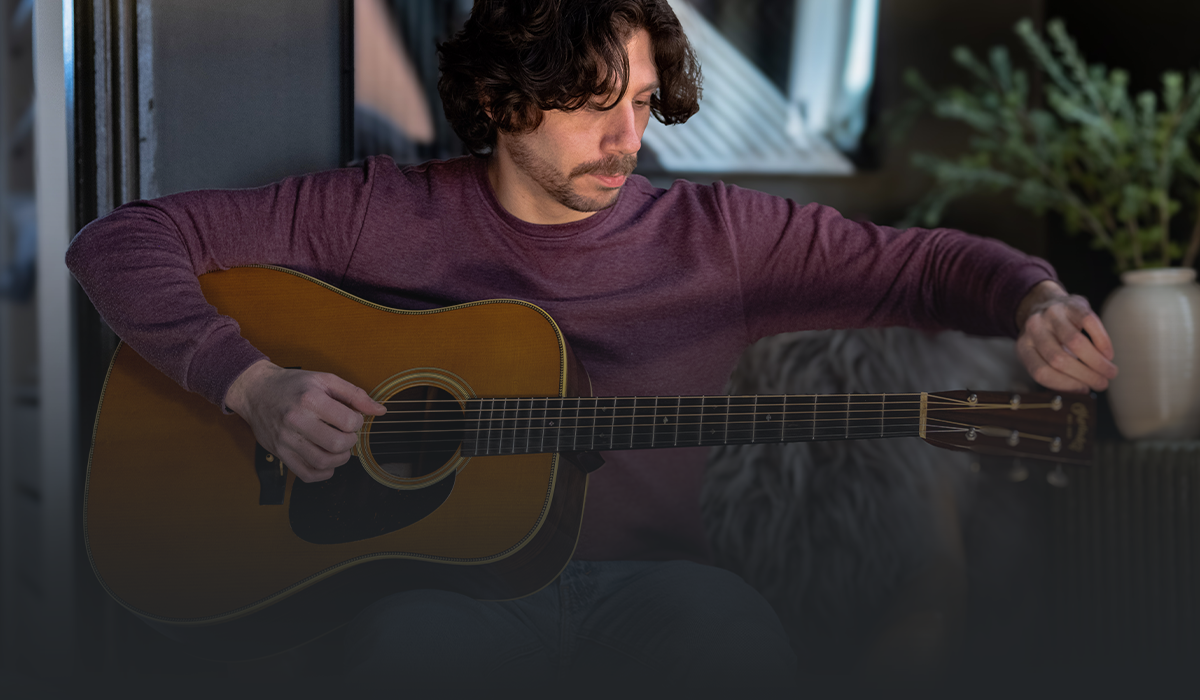 Man sitting indoors carefully tuning an acoustic guitar