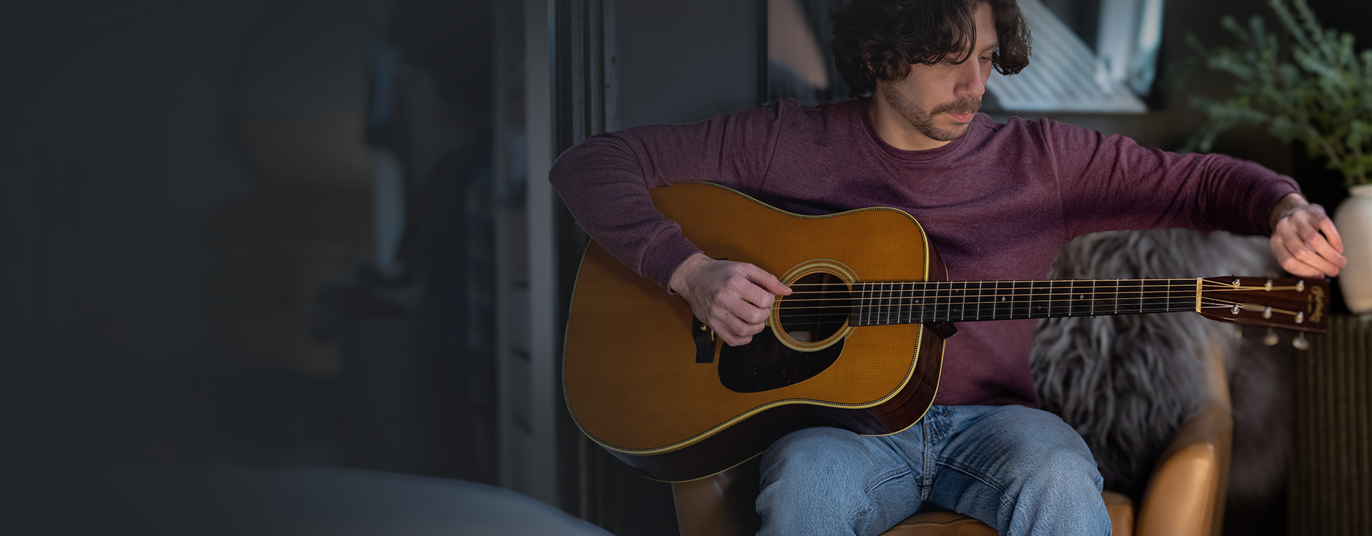 Man sitting indoors carefully tuning an acoustic guitar