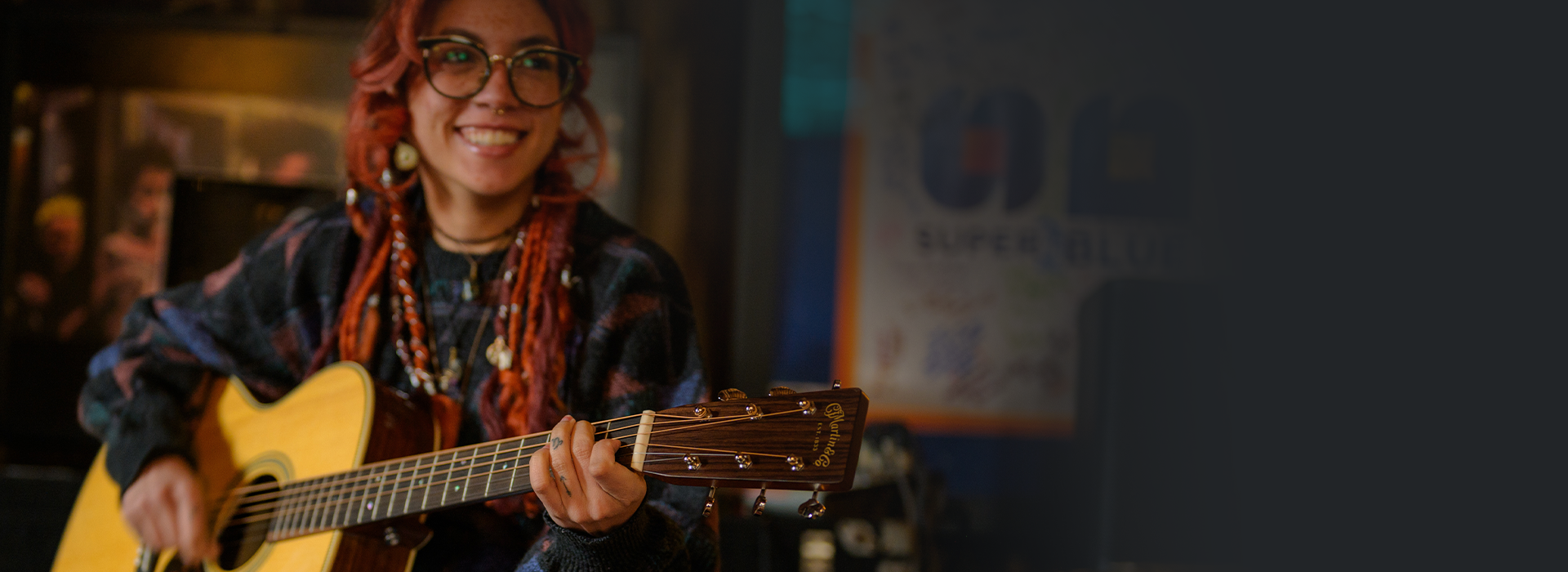 Musician smiling while playing an acoustic guitar in a relaxed indoor setting