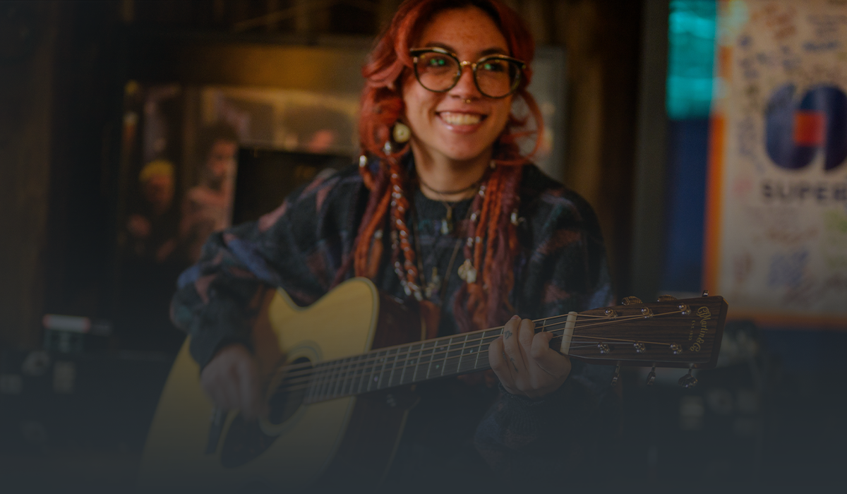 Musician smiling while playing an acoustic guitar in a relaxed indoor setting