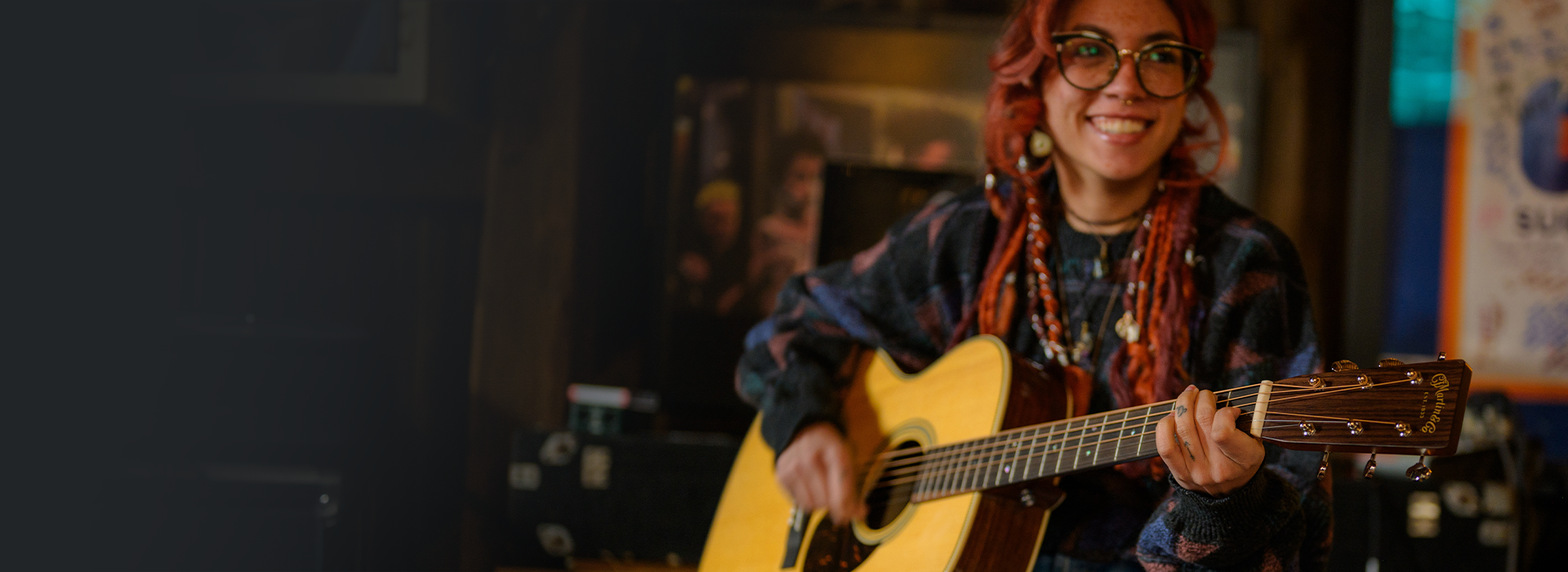 Musician smiling while playing an acoustic guitar in a relaxed indoor setting