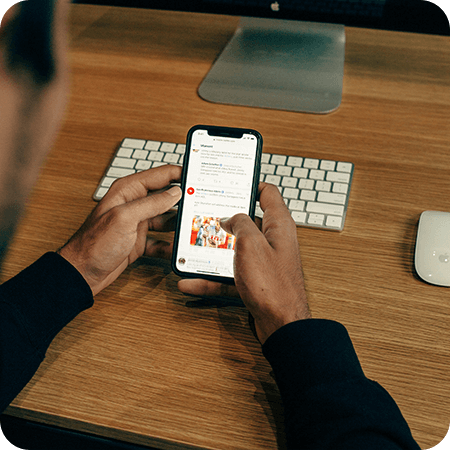 Hands holding a phone and scrolling at a workspace