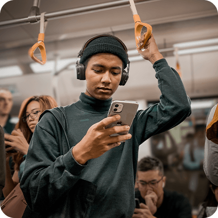 Person standing on public transit wearing headphones and looking at their phone.