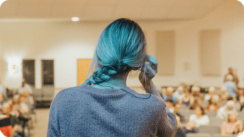 Person preparing to speak on stage in front of a seated audience.